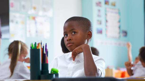 male elementary school pupil wearing uniform working at desk
